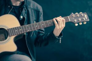 Home Close-up of a musician playing an acoustic guitar, wearing a leather jacket.