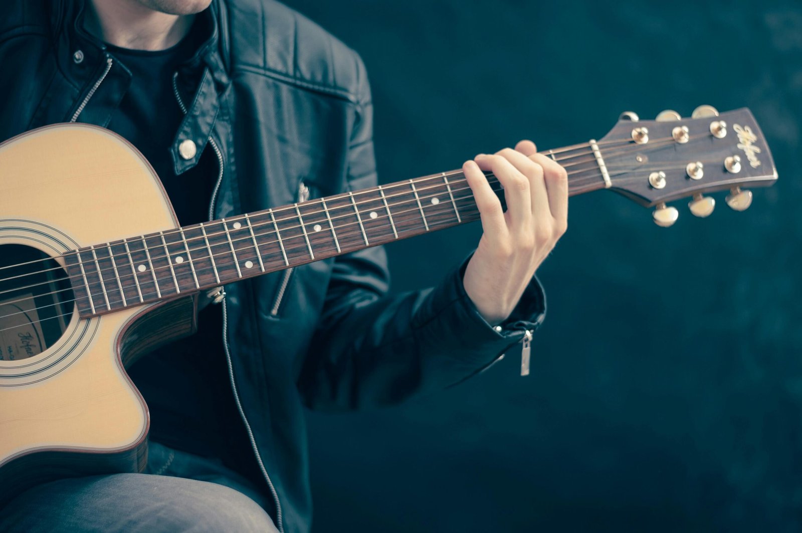 Home Close-up of a musician playing an acoustic guitar, wearing a leather jacket.